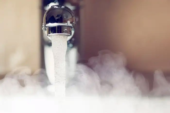 A tap turned on with water running and steam all around